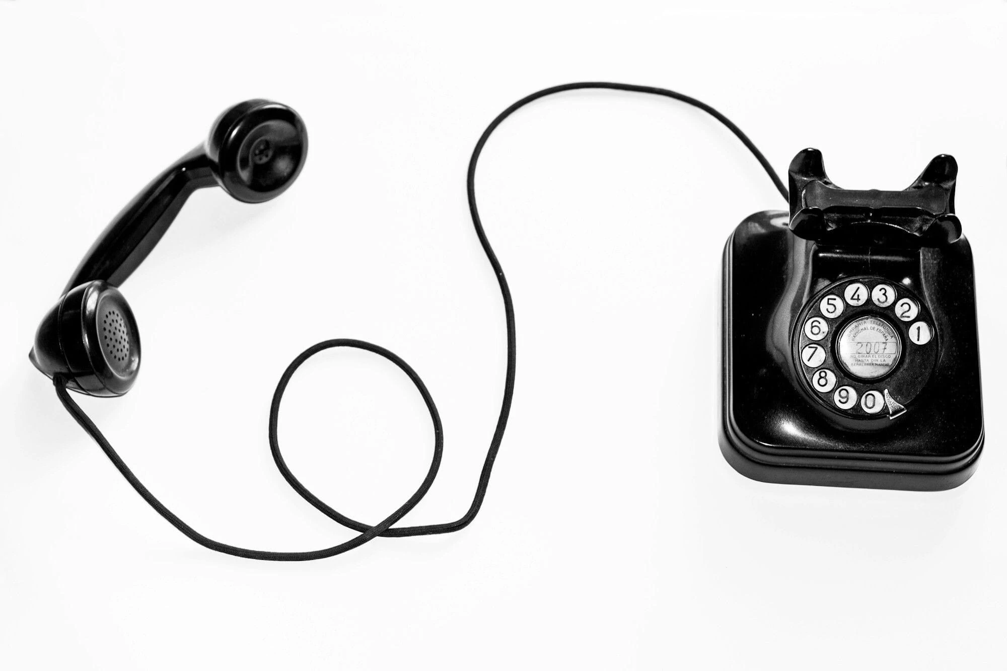 Bildet synar ein gamaldags, svart telefon. Telefonen har dreieskive. Telefonrøyret ligg eit stykke til venstre for telefonen og det er krøll på ledninga.